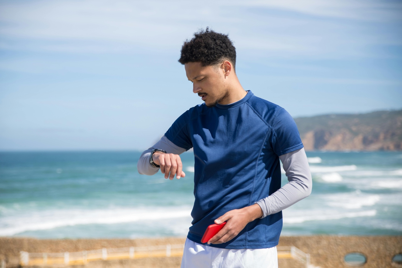 A man in a blue shirt looking at his wristwatch against an ocean shore