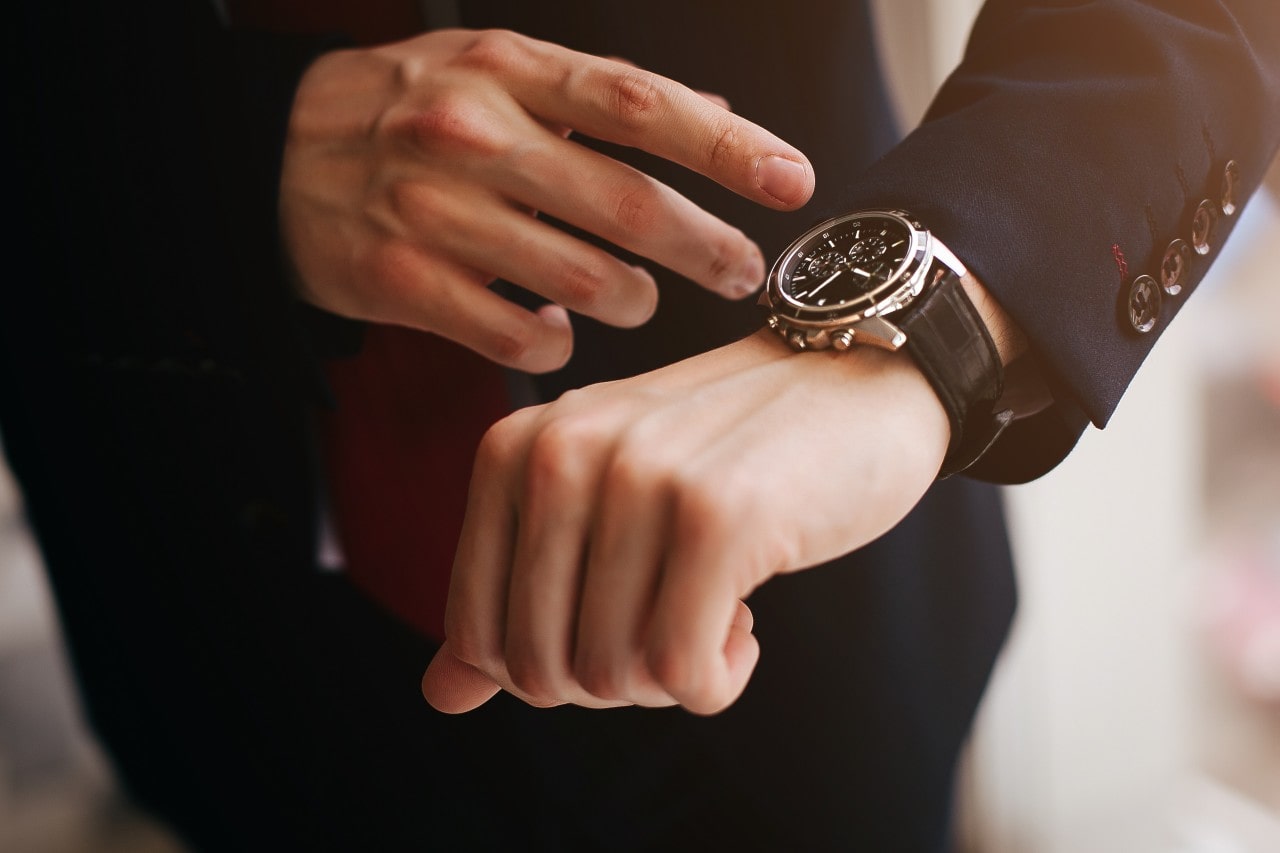 a man in a black suit reaching down to his silver and black watch
