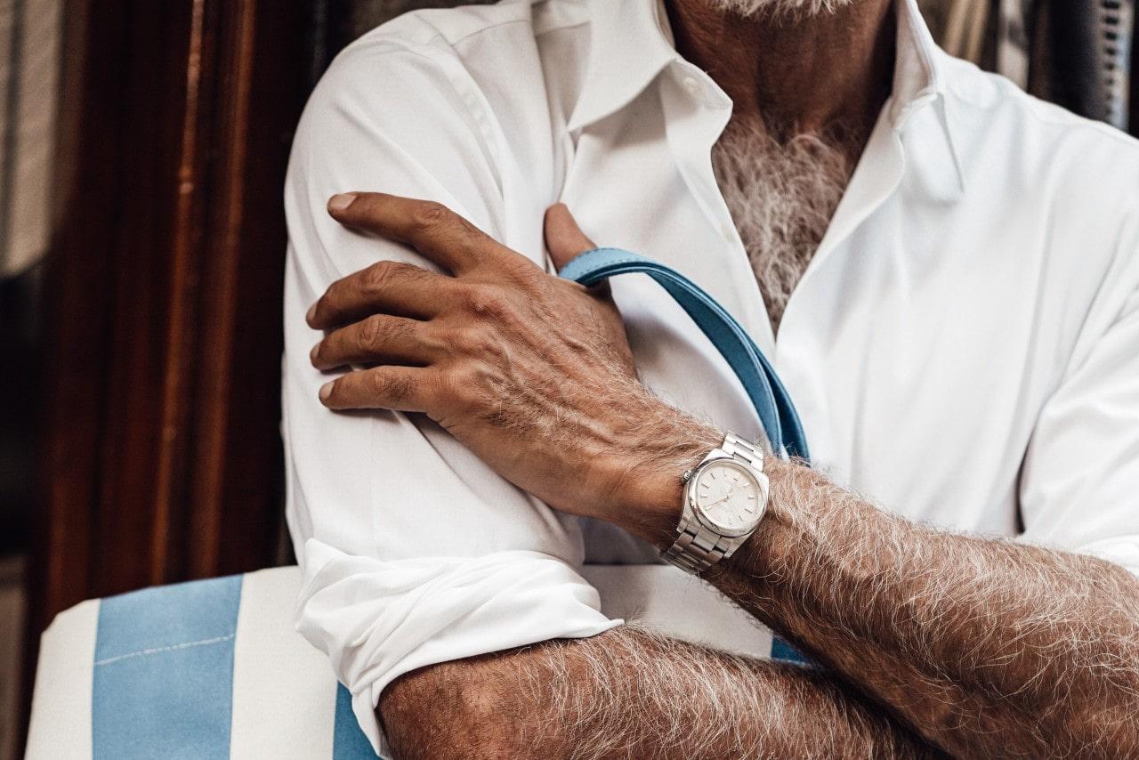 an older man in a white shirt holding a striped bag and wearing a silver watch