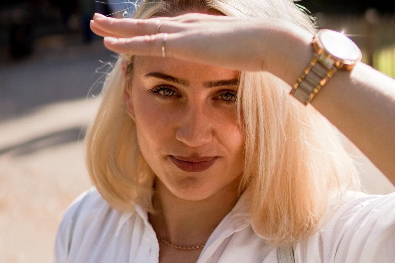 a woman with her hand raised to shade her eyes wearing a mixed metal watch