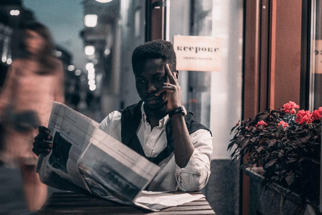 a man reading the paper outside a cafe and wearing a black strapped watch