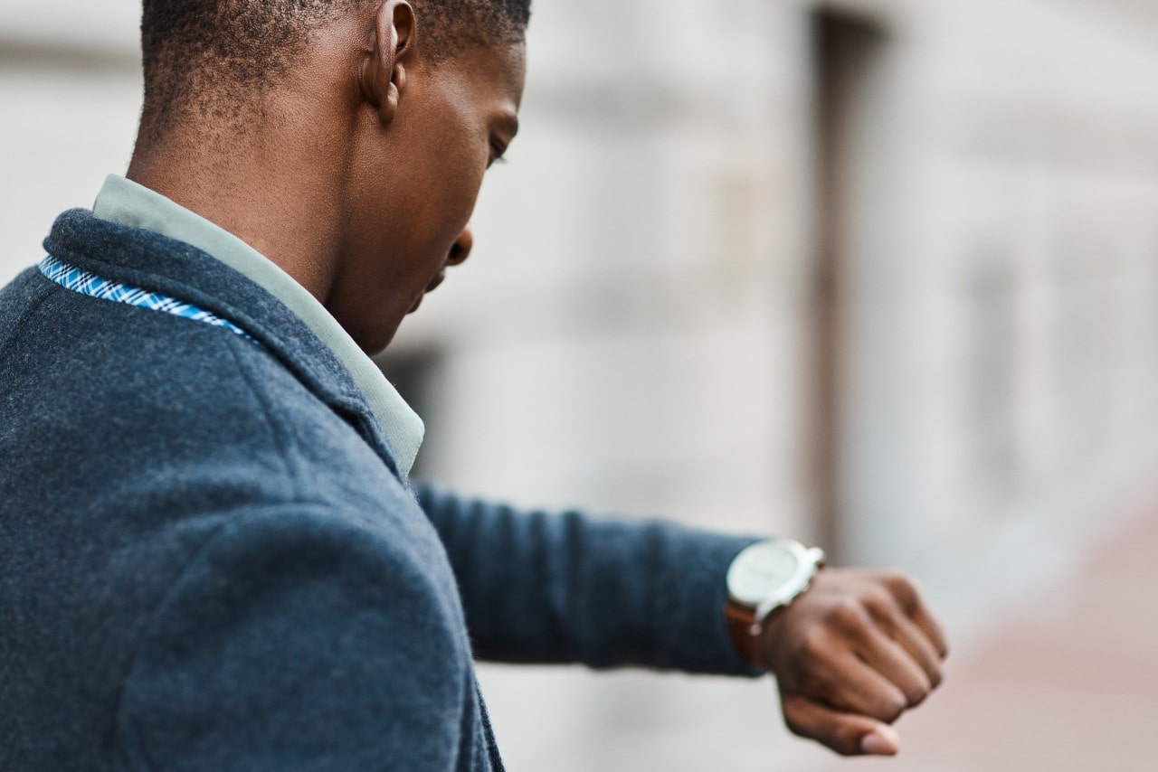 A man in a blue suit checking the time on his luxury watch.