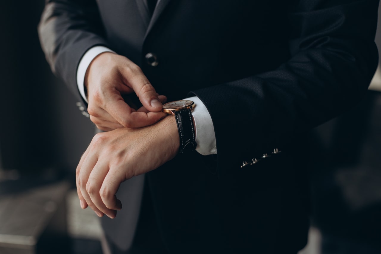 A man adjusting her dress watch that has a black leather strap.