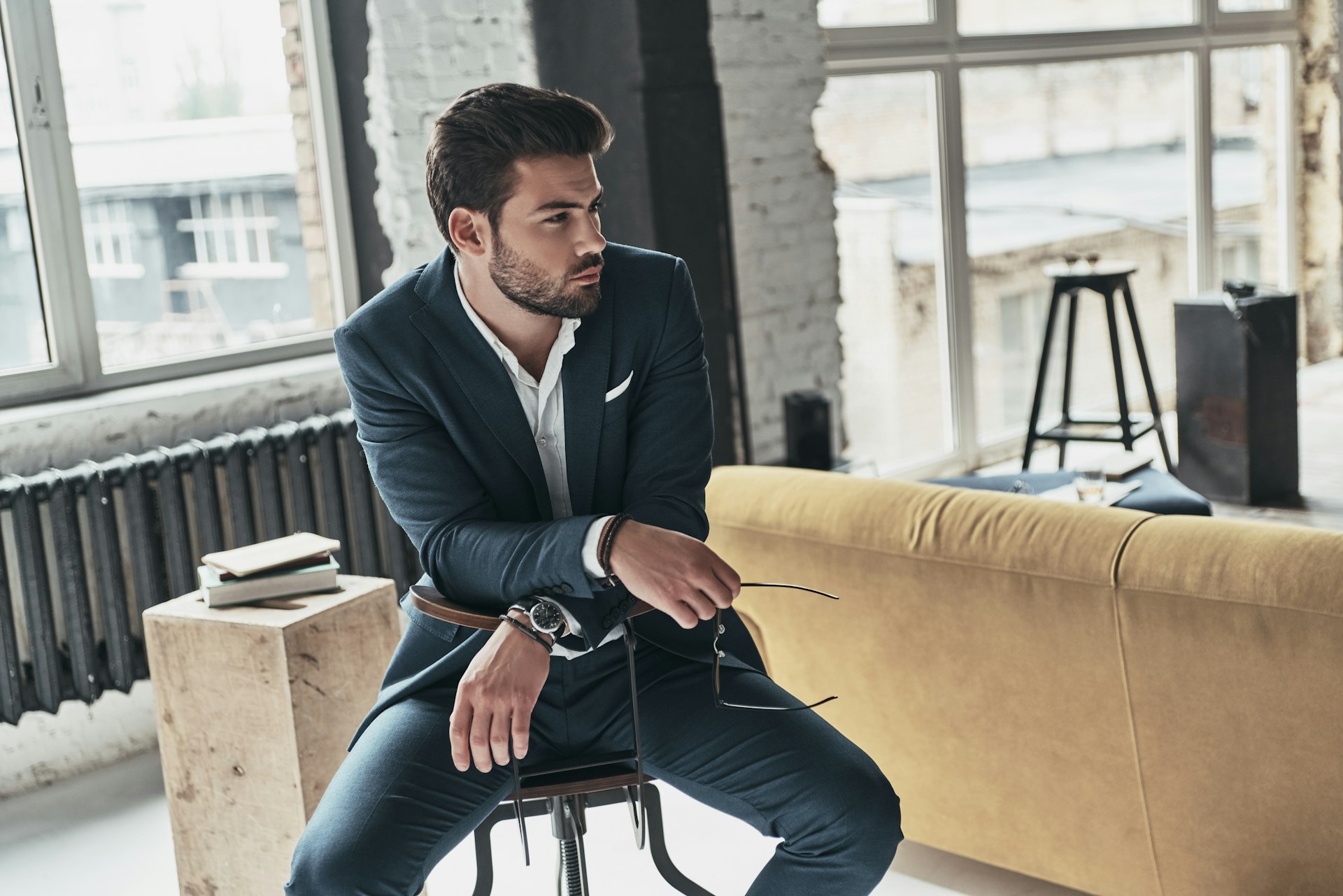 A well-dressed man sitting backwards on a chair in a suit wearing a luxury watch