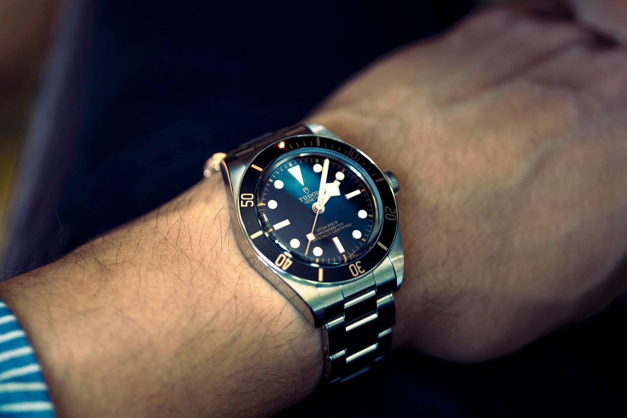 A close-up image of a man’s wrist adorned with a silver, black, and gold TUDOR watch
