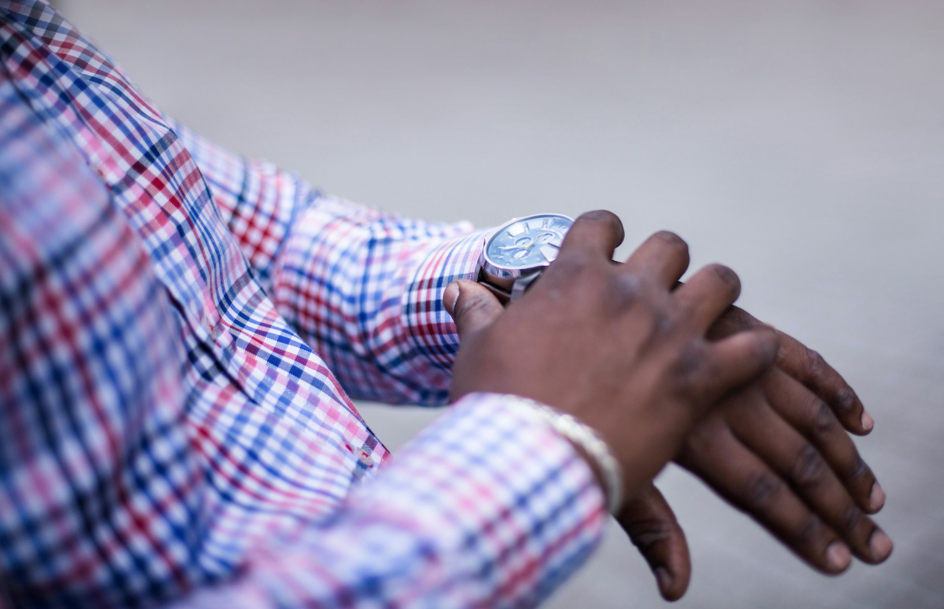 A man in a plaid shirt examining his silver dress watch.
