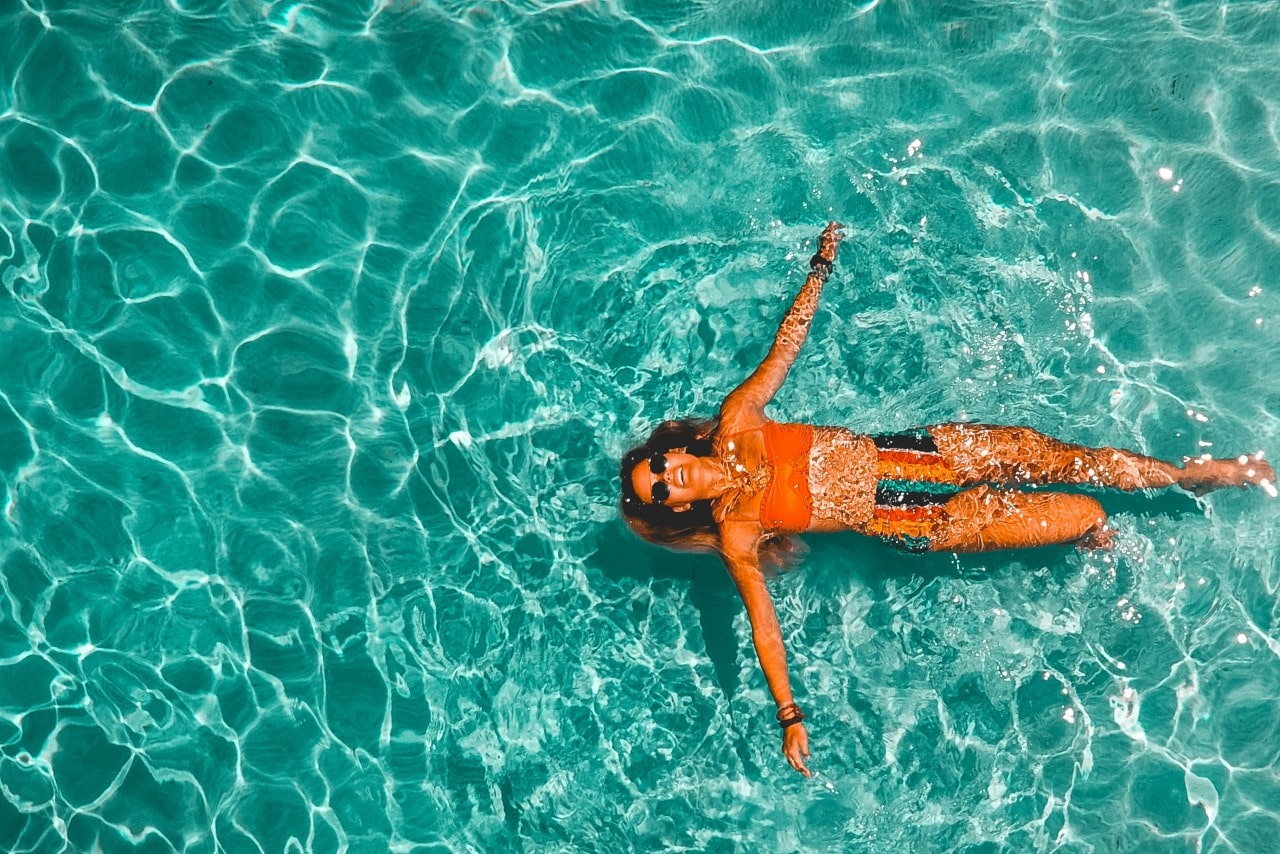 a woman floating in the water wearing a bright swimsuit and black watch