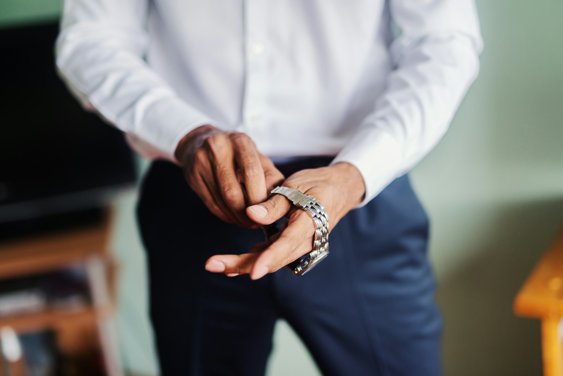 A close-up of a man putting a stainless steel dress watch on his wrist.