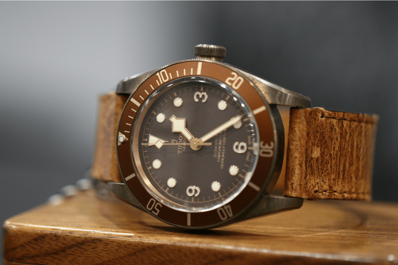 A close-up image of a vintage-style TUDOR watch on a wooden surface.