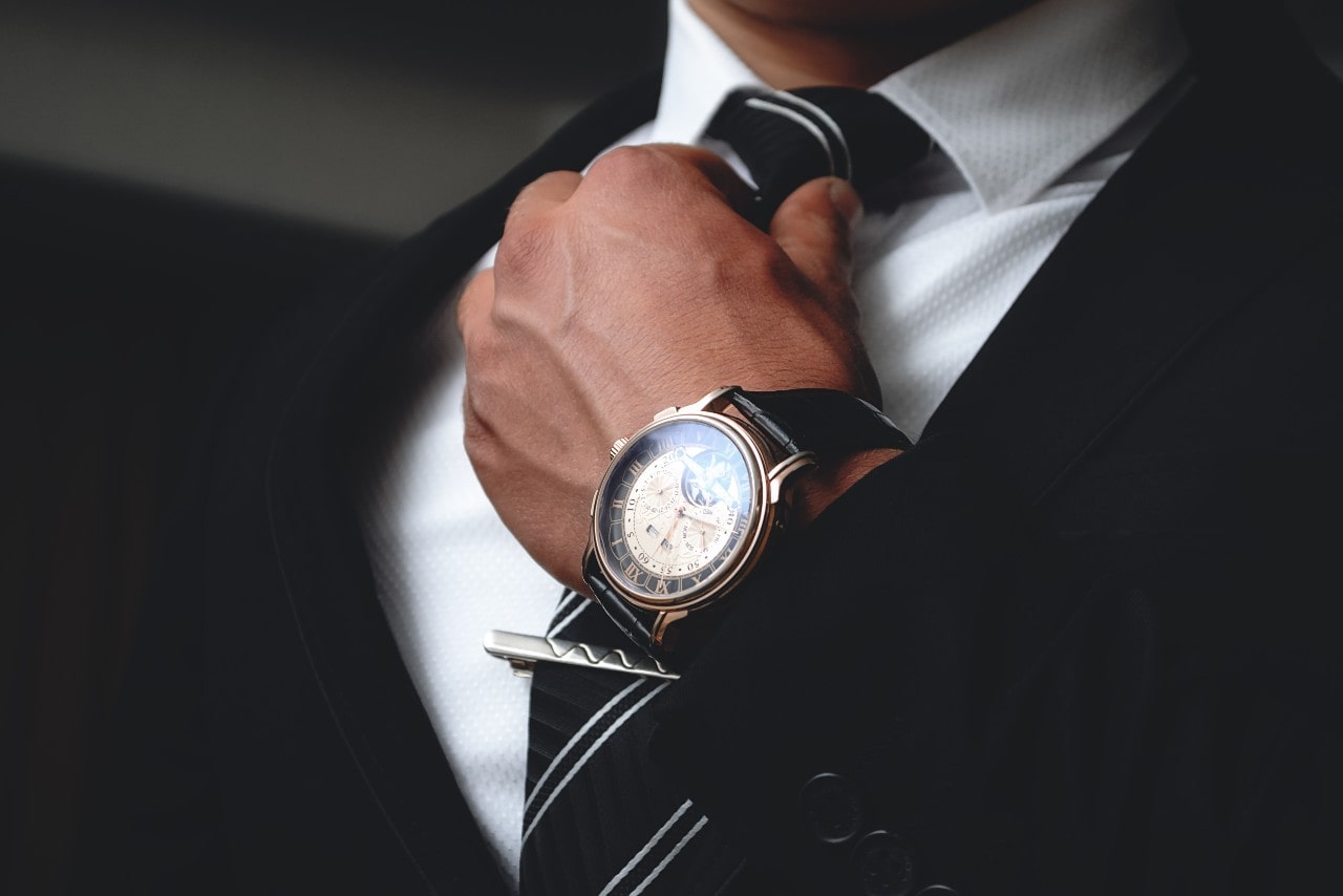 A close-up of a well-dressed man’s hand, clad with a luxury watch, adjusting his tie. A close-up of a well-dressed man’s hand, clad with a luxury watch, adjusting his tie.