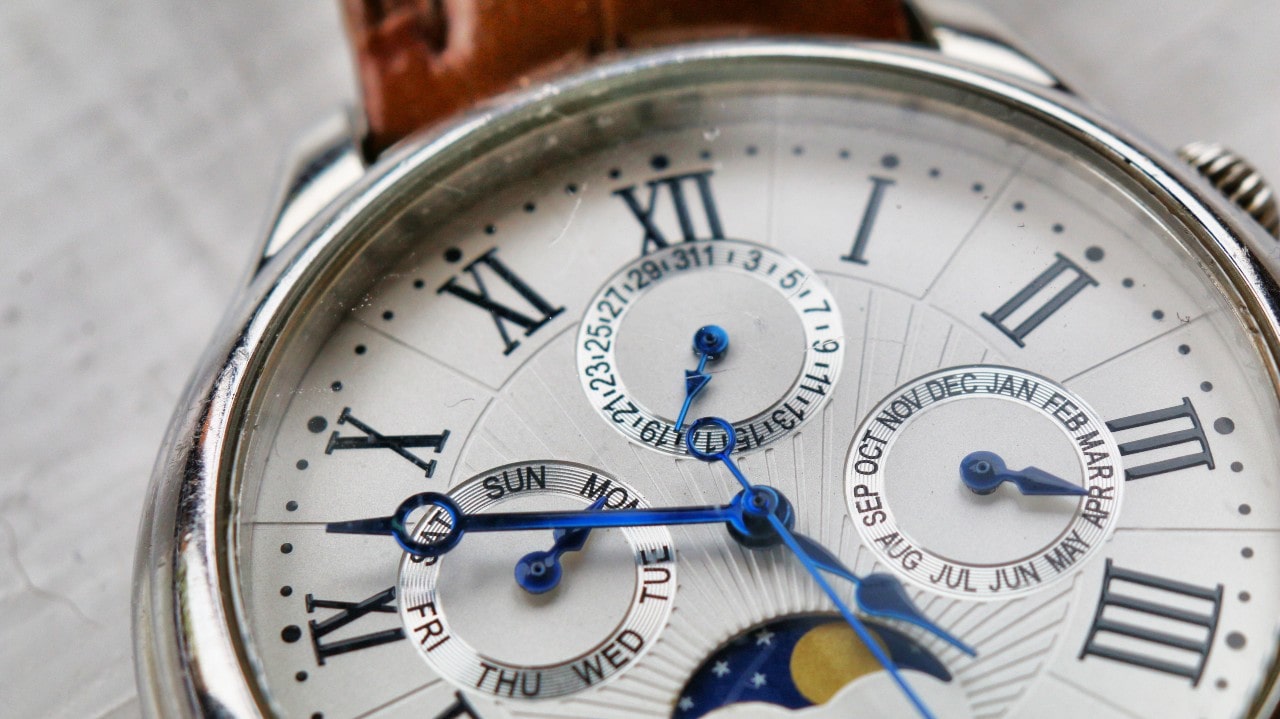 A close-up of a watch dial featuring Roman numerals and multiple subdials, with blue hands and intricate detailing. A close-up of a watch dial featuring Roman numerals and multiple subdials, with blue hands and intricate detailing.